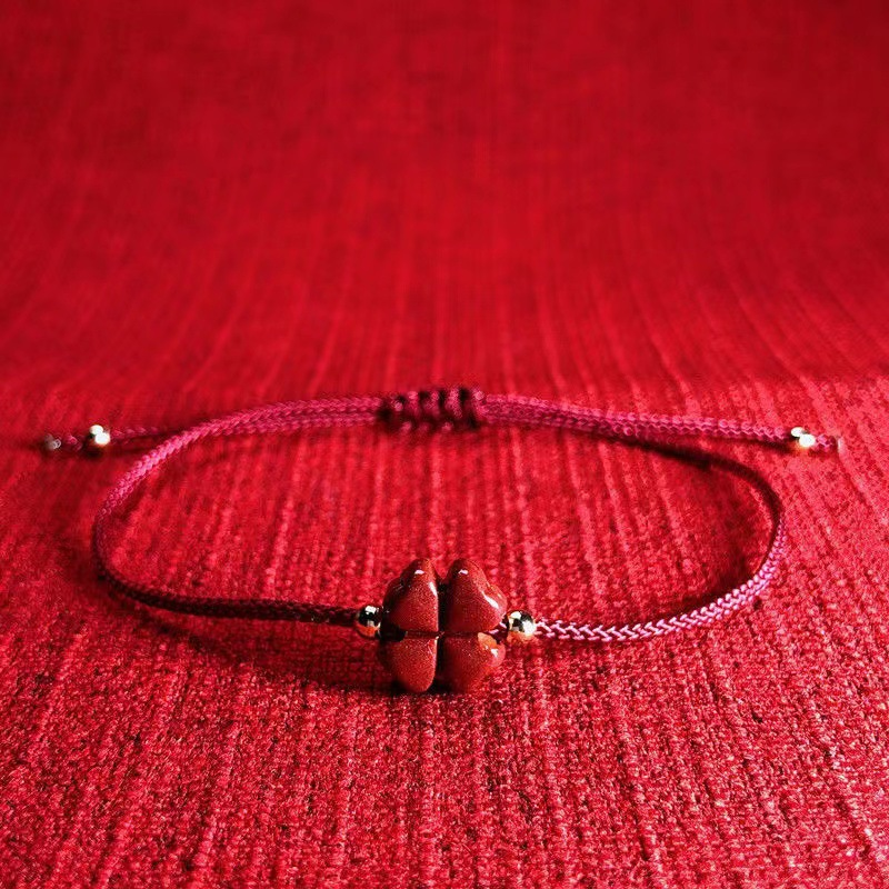 Close-up of the cinnabar four-leaf clover charm on the red string bracelet anklet