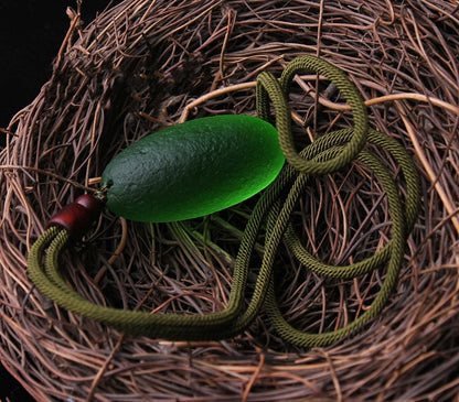 Green meteorite pendant necklace displayed in a hay nest, symbolizing nature, protection, and cosmic energy