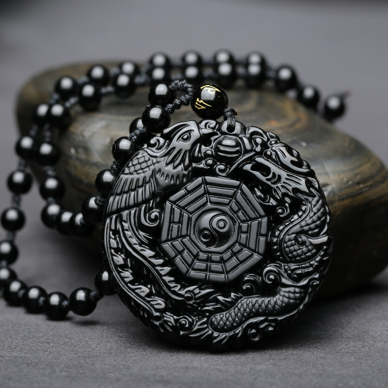 Close-up of carved dragon and phoenix on obsidian pendant necklace, showcasing intricate design