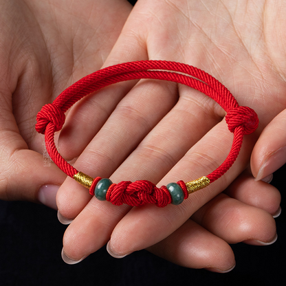 Red string jade lover's knot bracelet worn on the hand, showing its delicate design