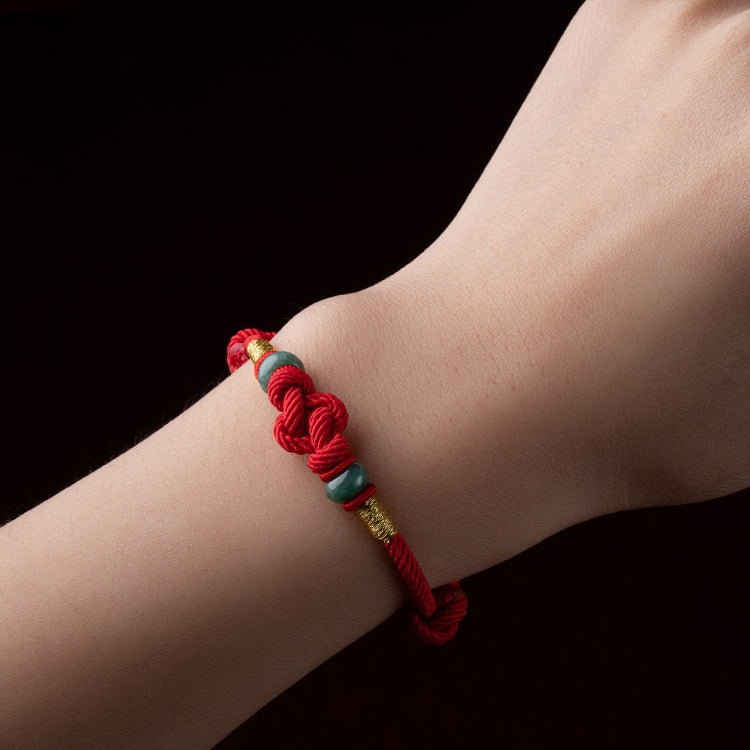 Red string jade lover's knot bracelet worn by a person, displaying its unique design