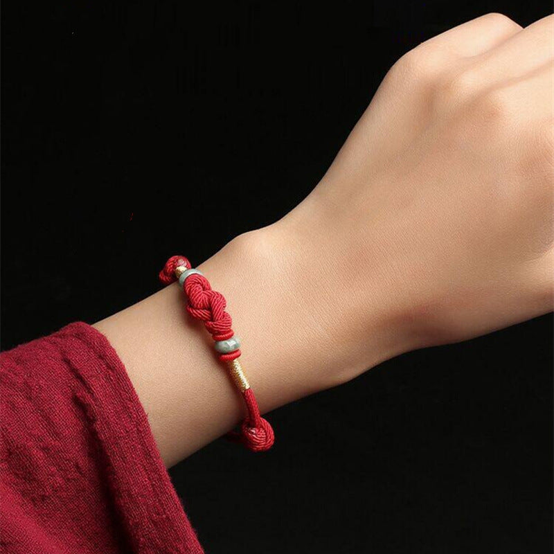 Red string jade bracelet on wrist, featuring the lover's knot and jade beads